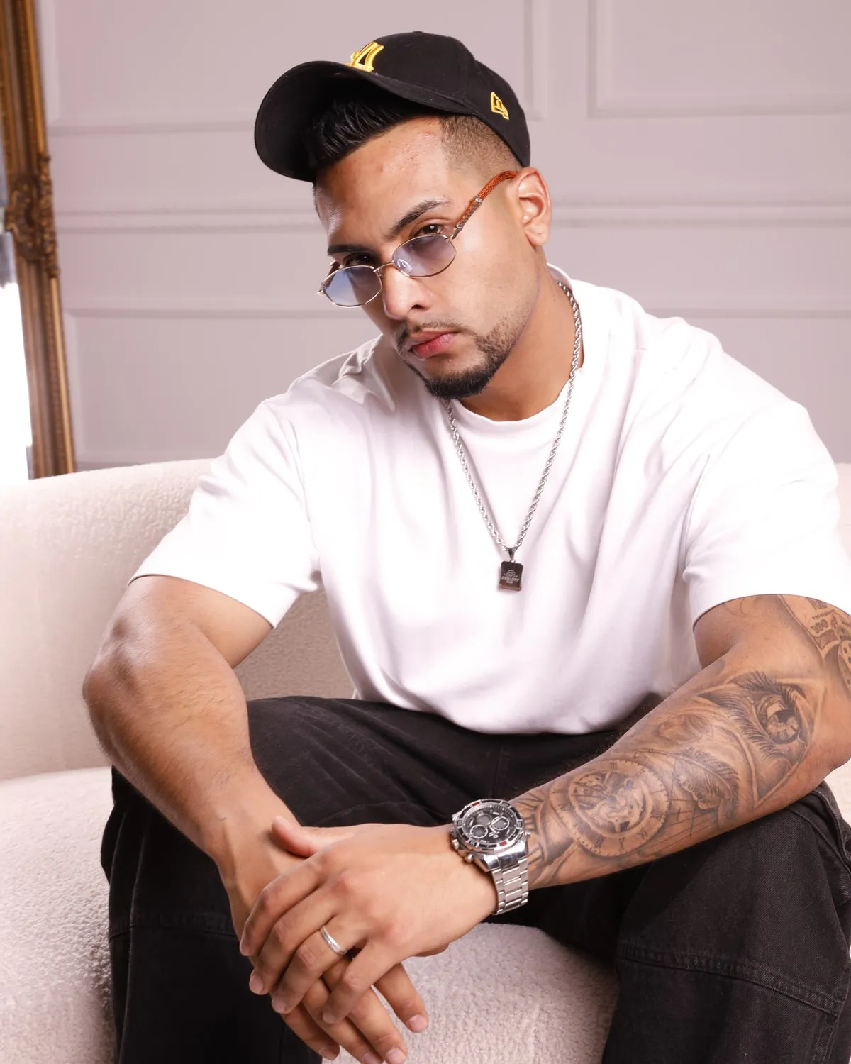 VaronW de cerca, con gorra negra, gafas de cristal azul, cadena y reloj